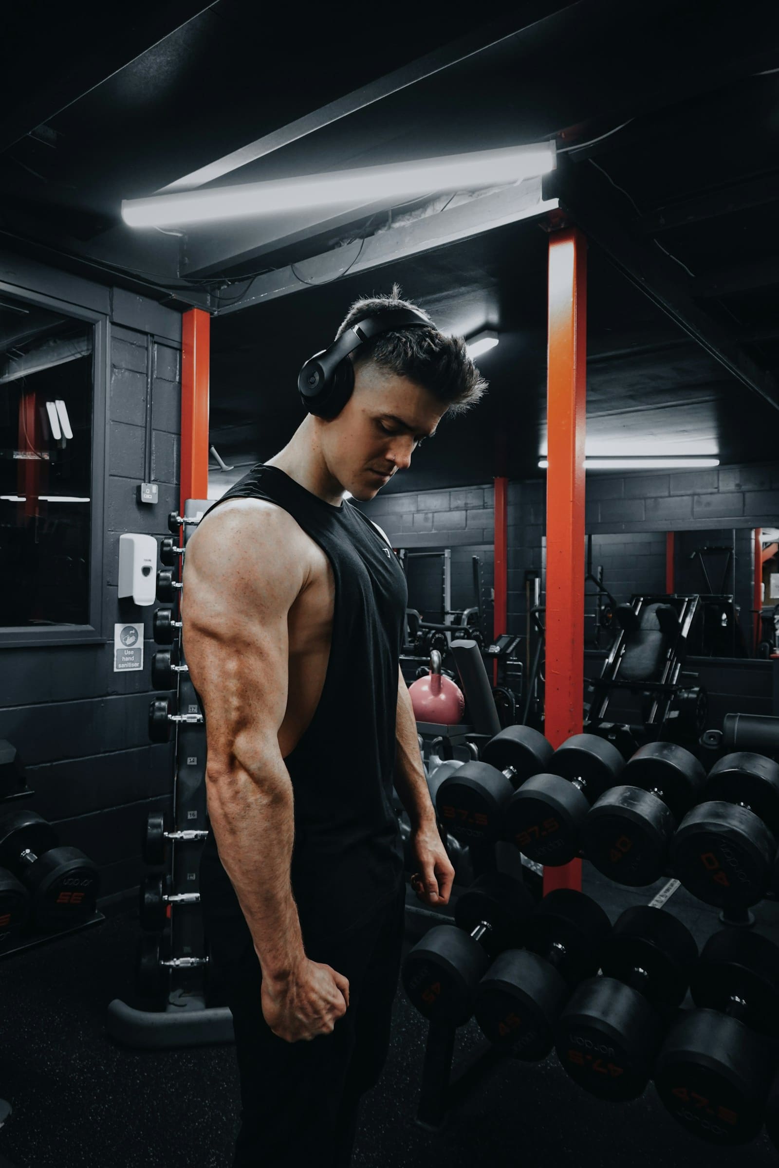 A member at the dumbbell rack, headphones on, between sets